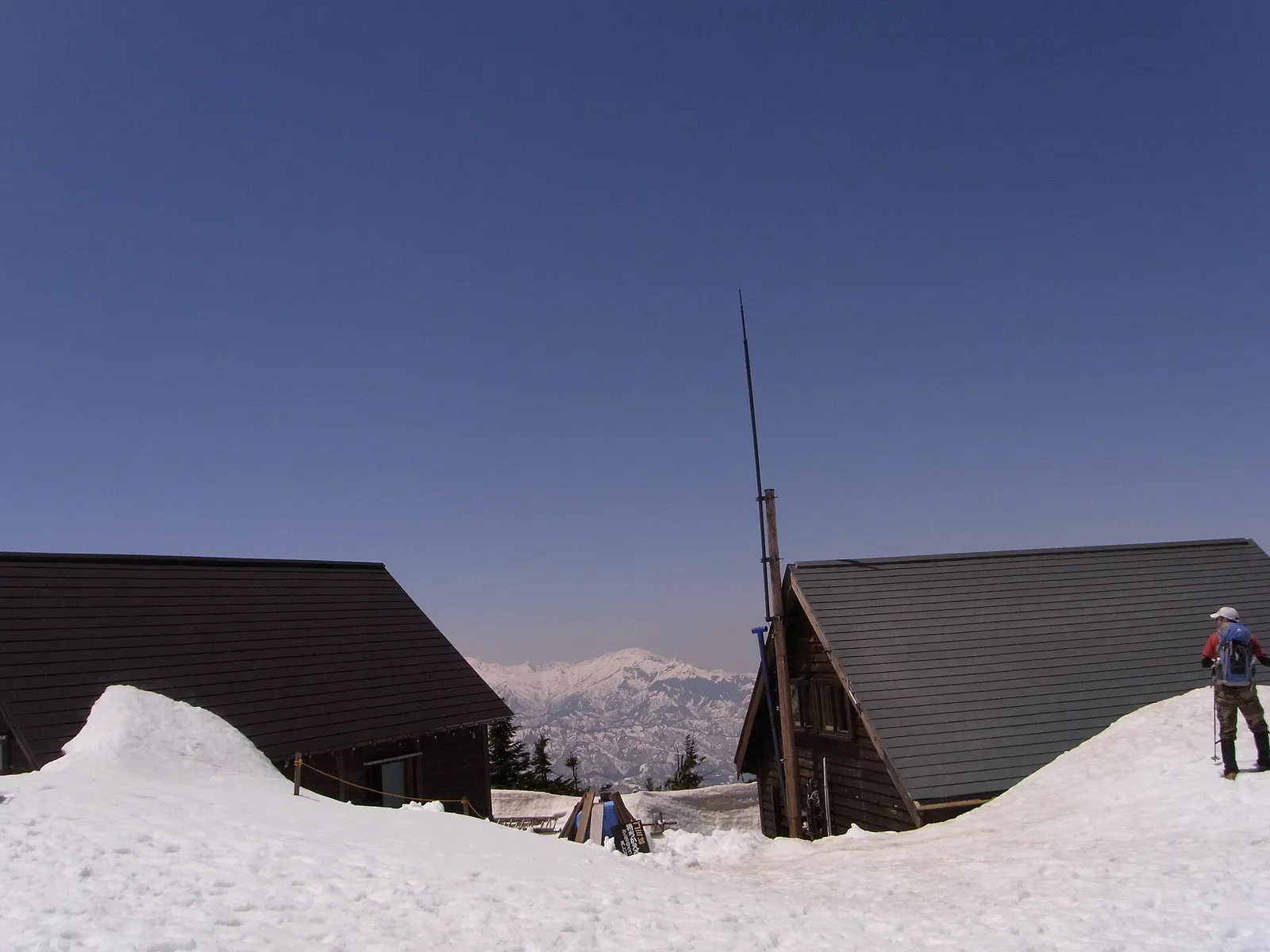 雪に囲まれた駒の小屋の建物と、奥に見える遠くの山並み