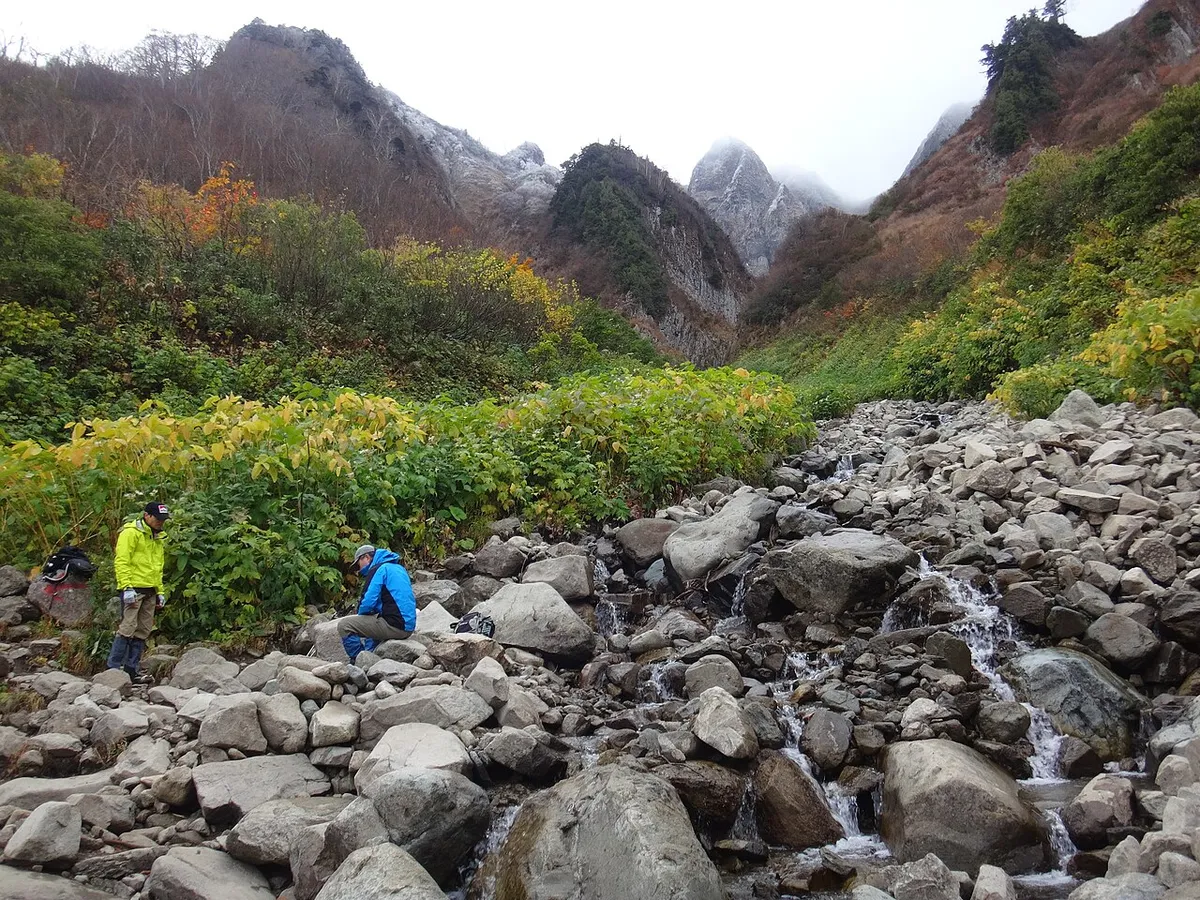荒菅沢の岩場で休む登山者と、周囲の紅葉