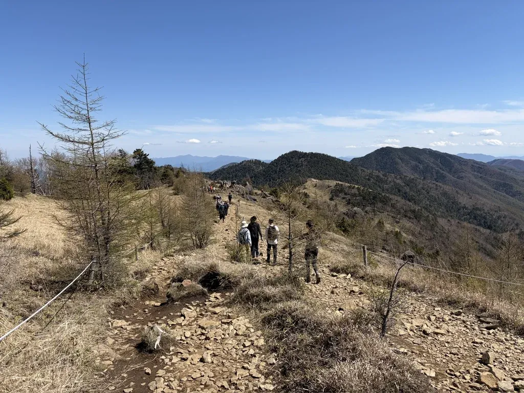 ロープが張られた草原の稜線を、大菩薩峠方面へ歩く登山者たち。まわりに高い木はない
