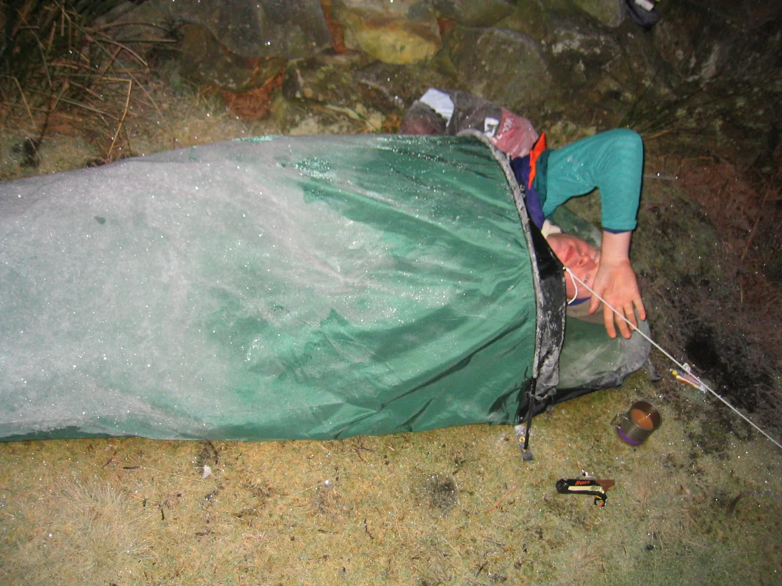 表面が凍りついた緑色のビバーク用シェルターに入り、岩陰で夜を明かした登山者