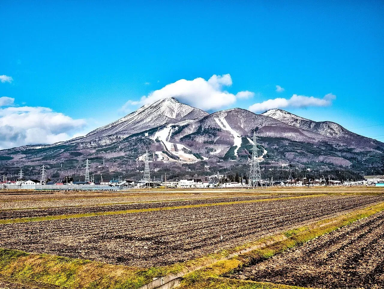 山頂部に雪をまとった冬の磐梯山と、手前の田畑