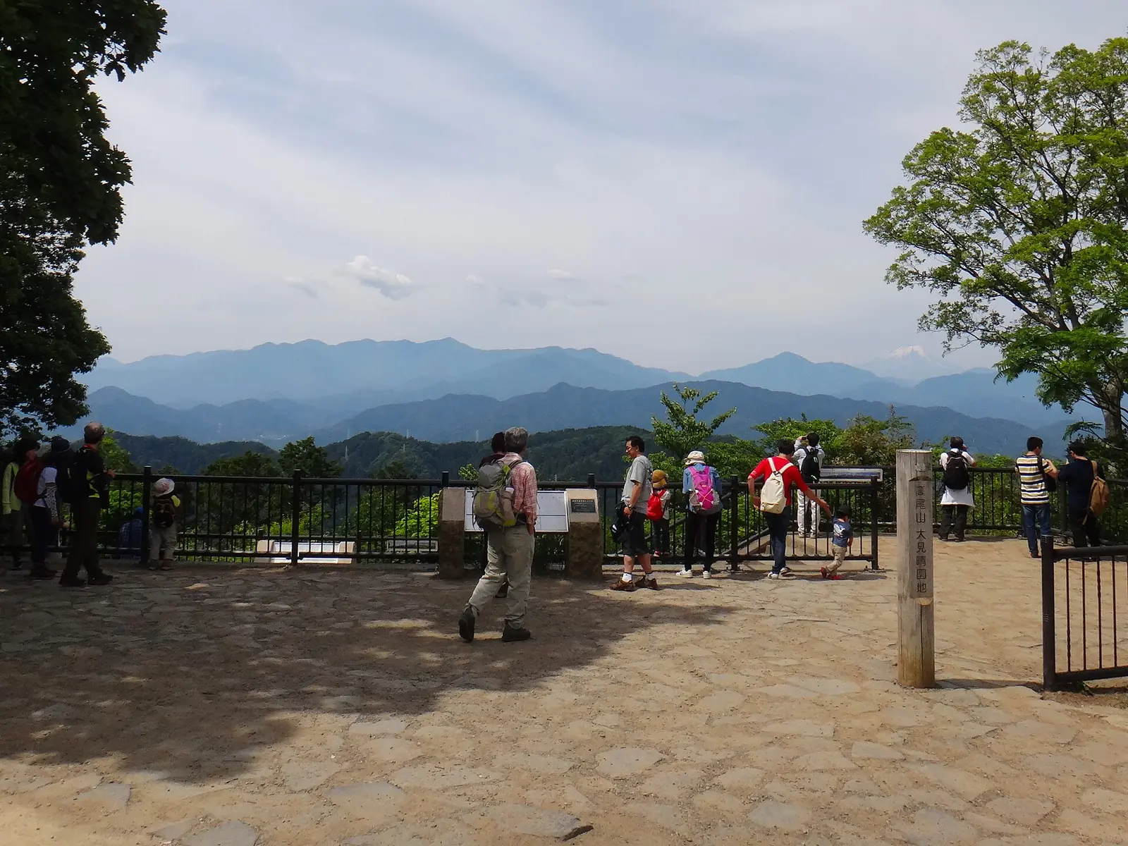 高尾山の山頂広場で、遠くの山並みを眺める大勢のハイカー