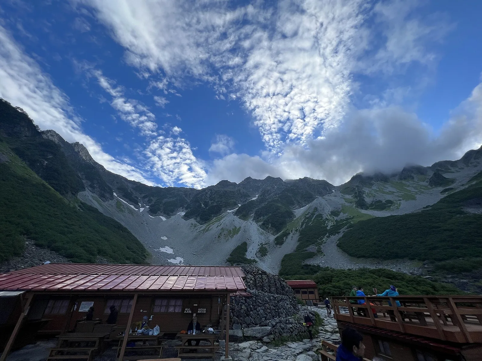 涸沢カールの山小屋の上に広がる奥穂高岳の岩稜と、筋状の雲が広がる青空