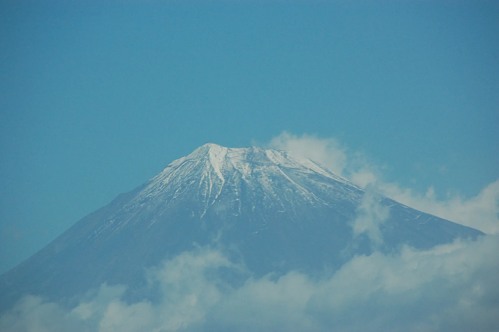 青空の下、山頂部が雪で白くなった富士山