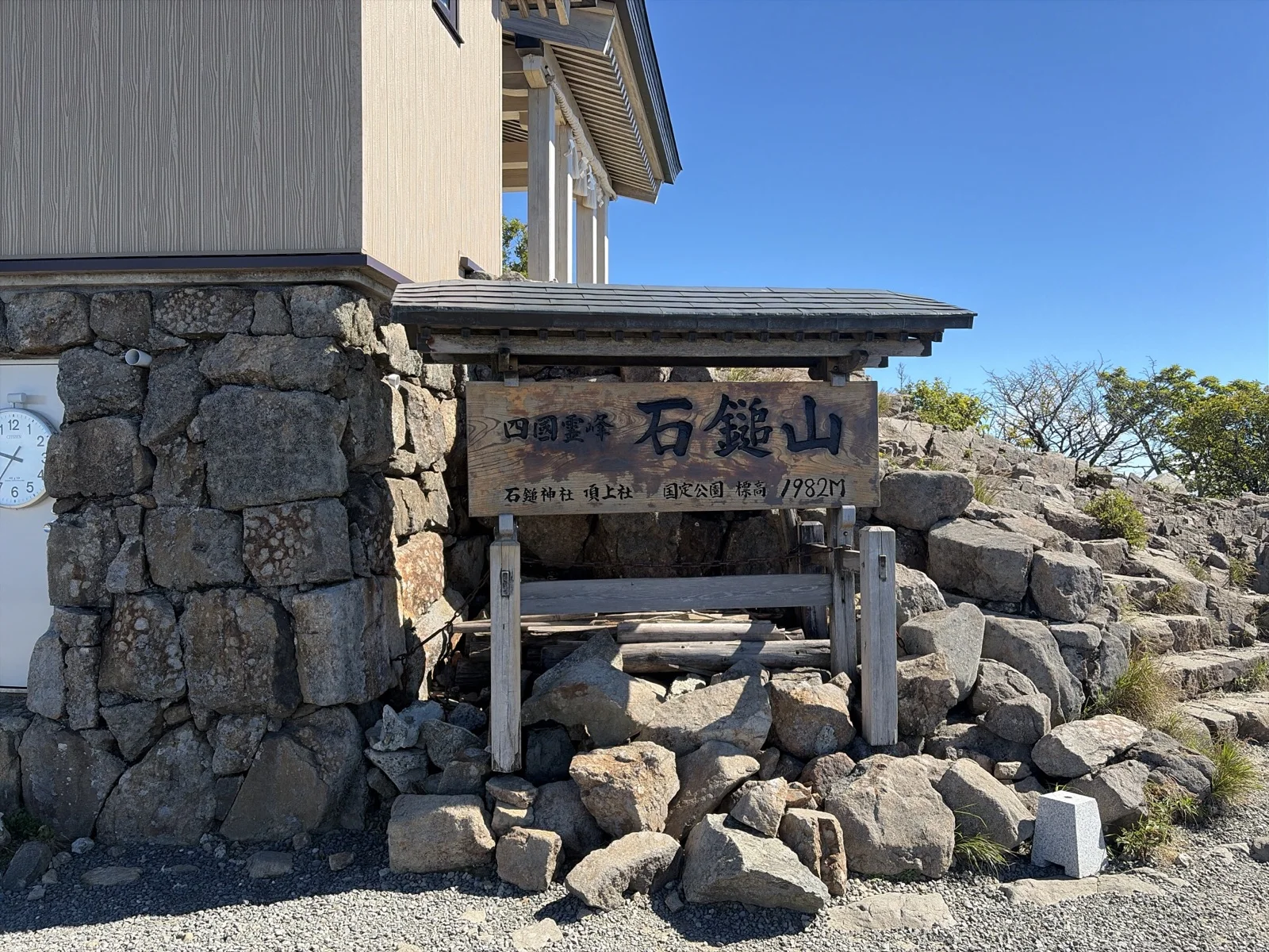 石鎚山・弥山山頂に立つ「四國霊峰 石鎚山 石鎚神社頂上社 国定公園 標高1982M」の木製看板と頂上山荘の石垣