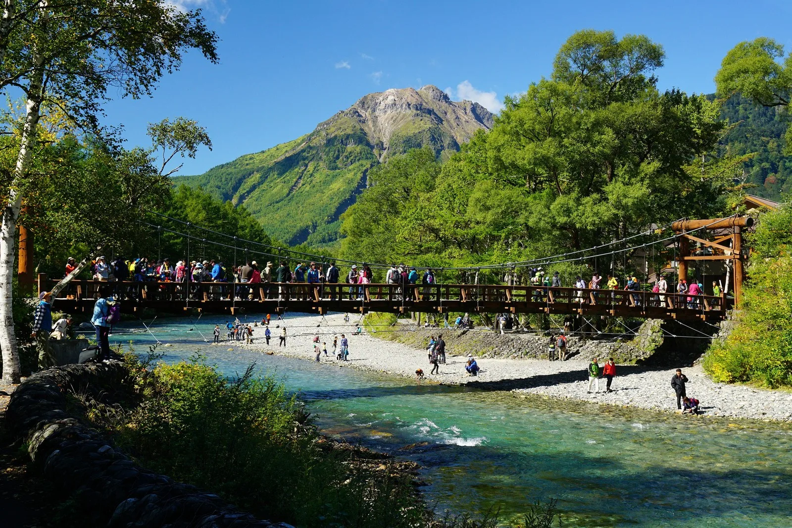 Wooden Kappa Bridge spanning the Azusa River with forested mountains and Mt. Yake in the background at Kamikochi