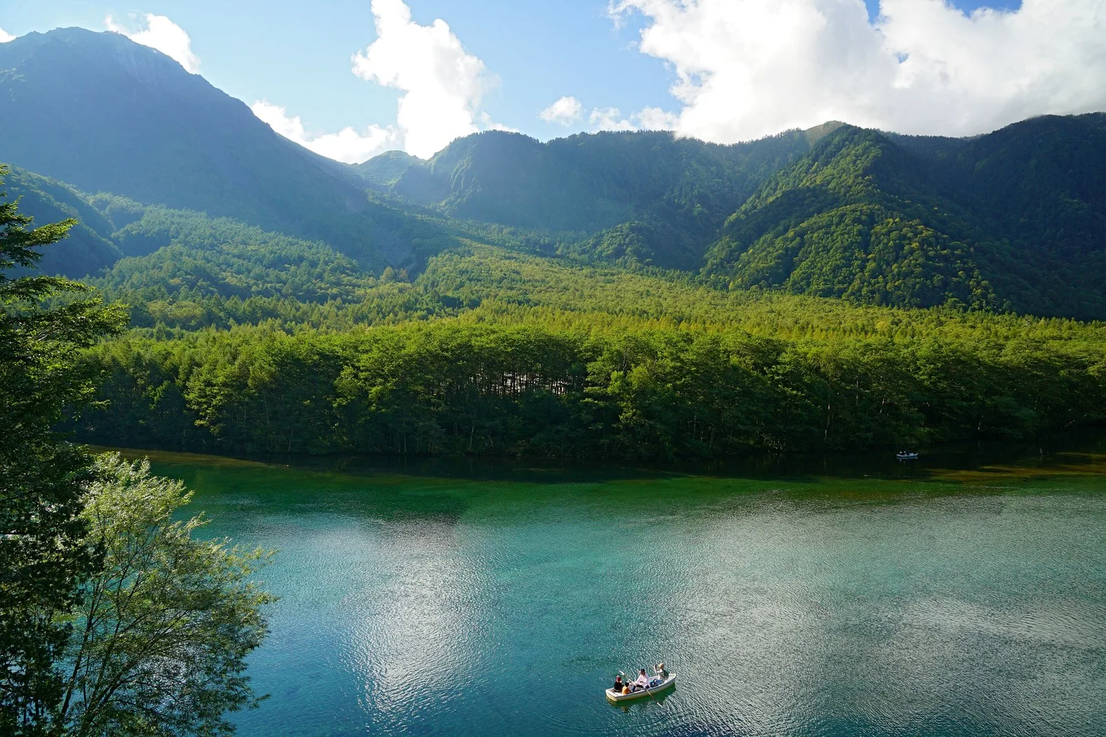 Calm water of Taisho Pond with dead standing trees and forested mountains at Kamikochi