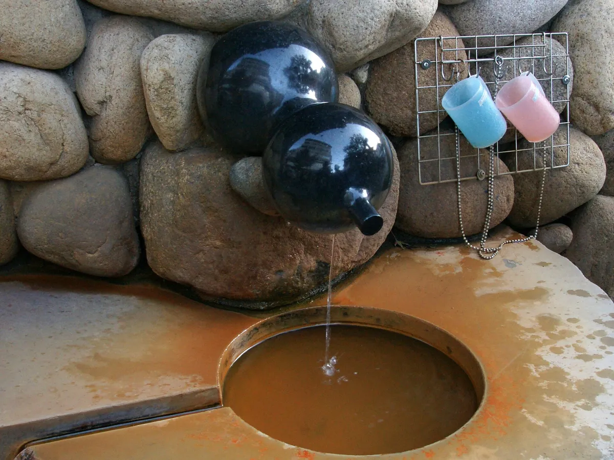 A stone basin filled with rust-brown kinsen hot-spring water outside Kin no Yu in Arima Onsen