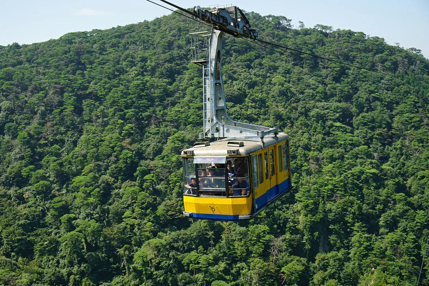 A yellow and blue Rokko-Arima Ropeway gondola passing over a forested slope