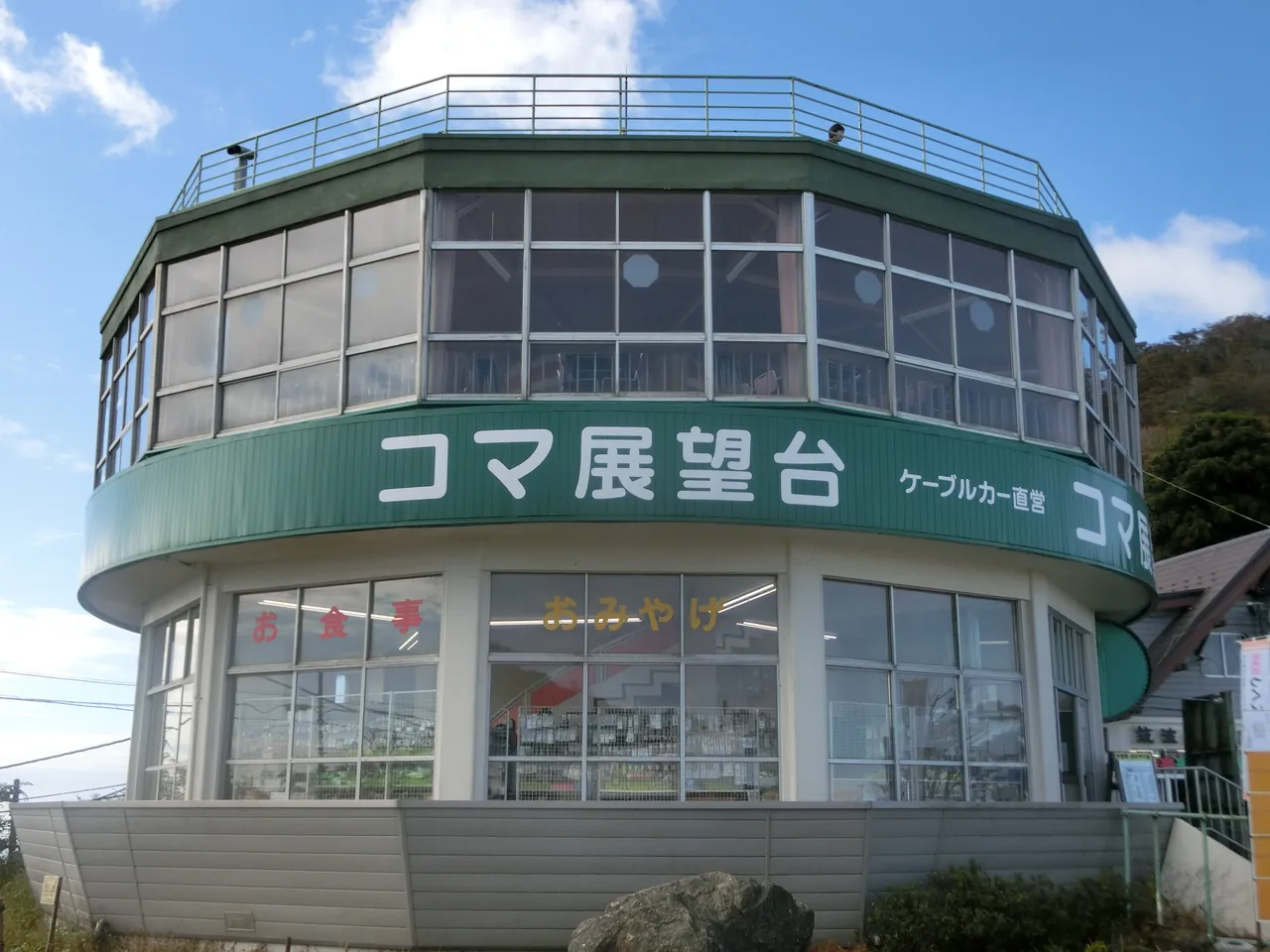 御幸原上一栋圆柱形的绿白色建筑，外墙写着「コマ展望台」，屋顶是展望台