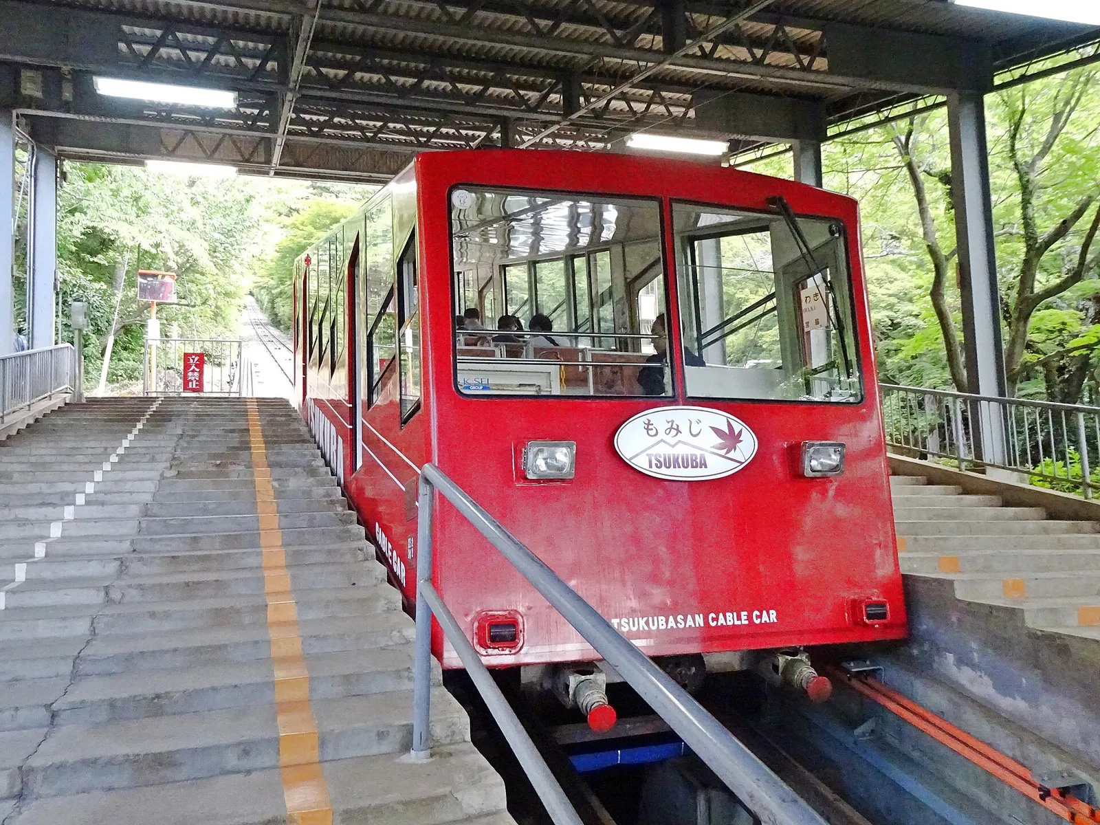The red Mt. Tsukuba Cable Car Momiji stopped at a station platform with stepped walkways on both sides