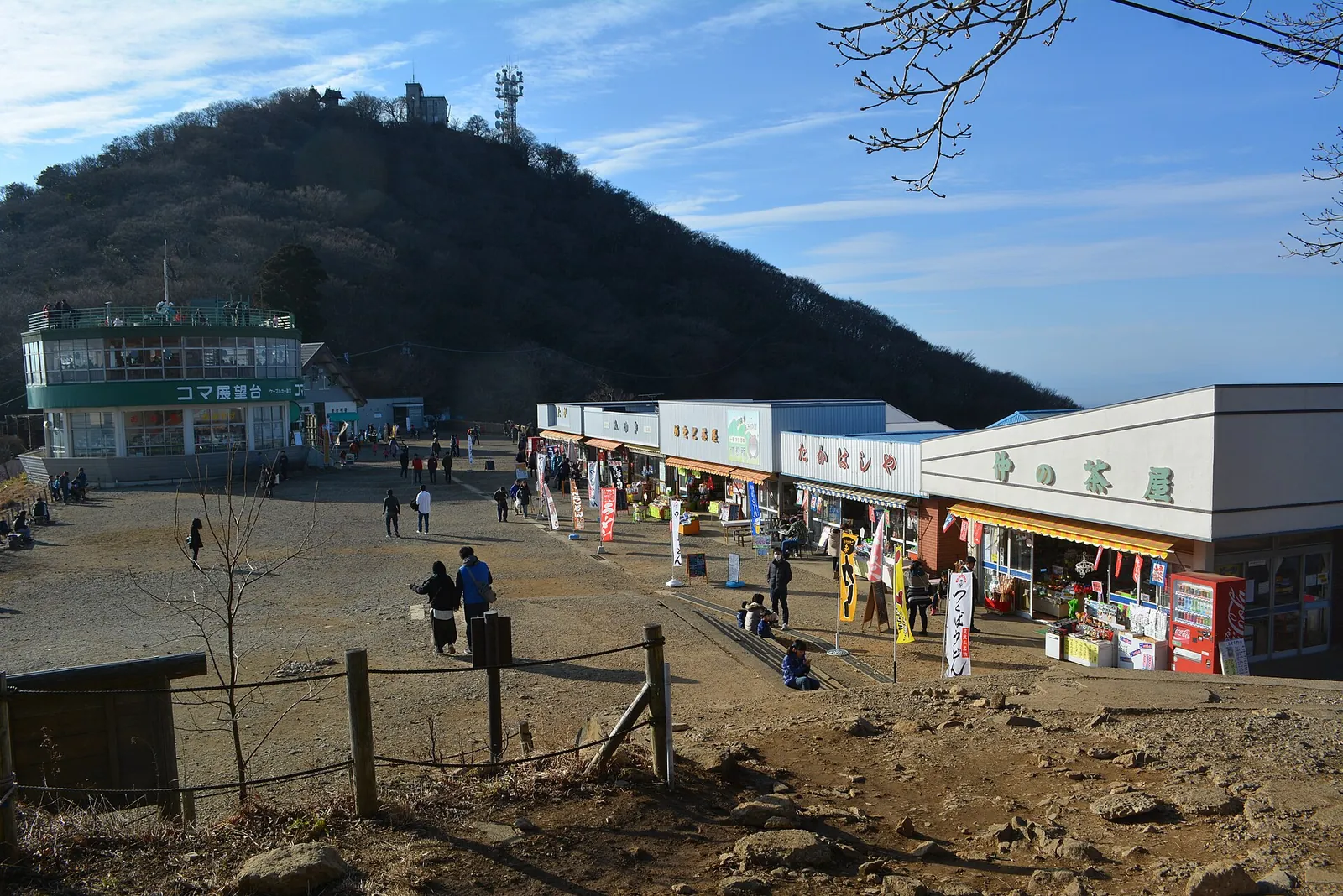 The open Miyukigahara saddle on Mount Tsukuba with a row of shops and visitors walking, and the forested Nantaisan peak behind