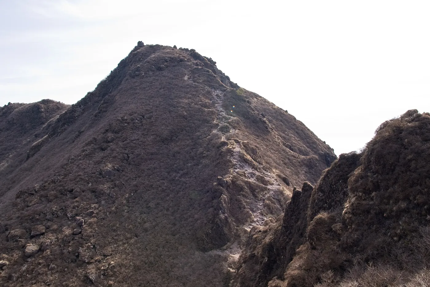 The rocky, steep-sided East Peak of Mount Yufu under a pale sky