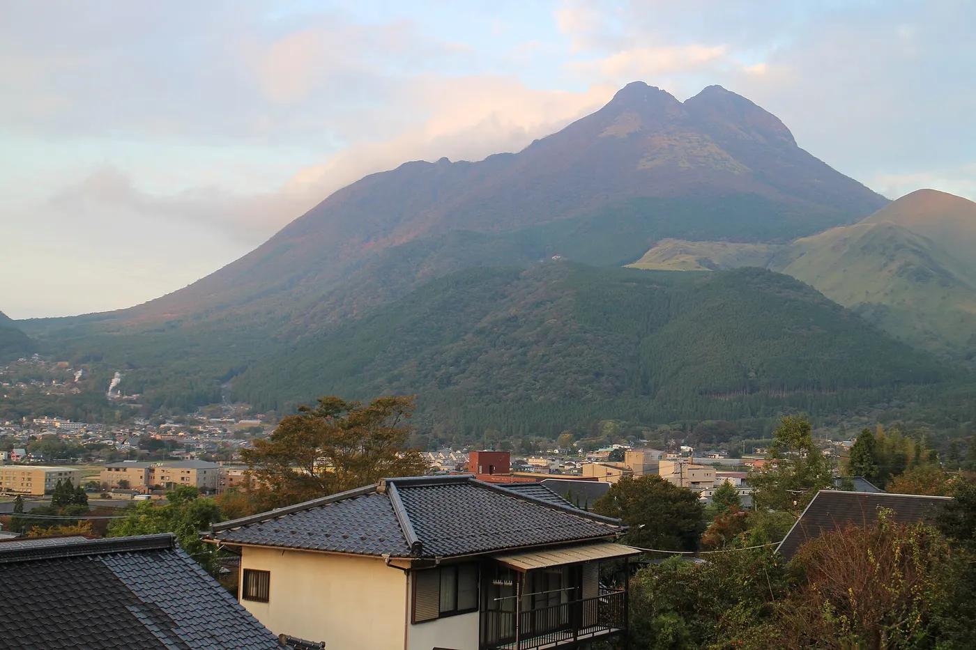 The twin summits of Mount Yufu rising above the tiled roofs and trees of Yufuin town in late afternoon light