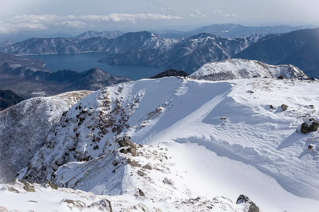 雪に覆われた日光白根山の山頂付近と遠くの湖と山並み