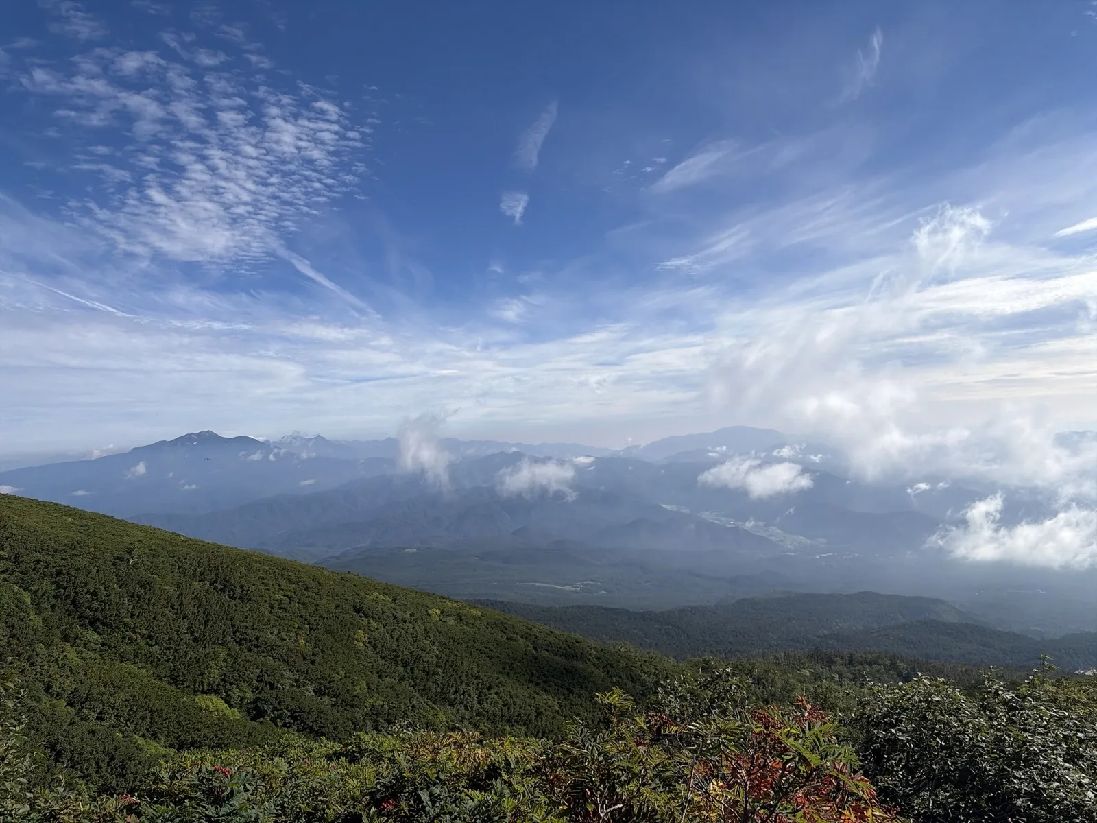 緑の斜面の向こうに、雲の下に連なる遠くの山並みが見える