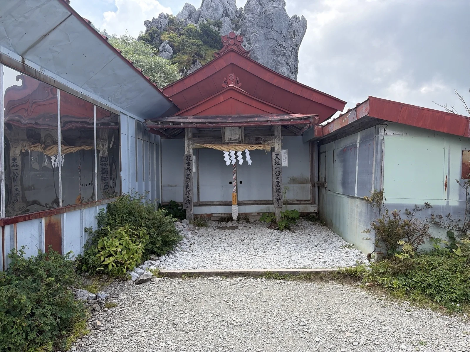 大剣神社の赤い屋根の社殿と、その背後に天を突くようにそびえ立つ巨大な岩塔・御塔石(おたていし)