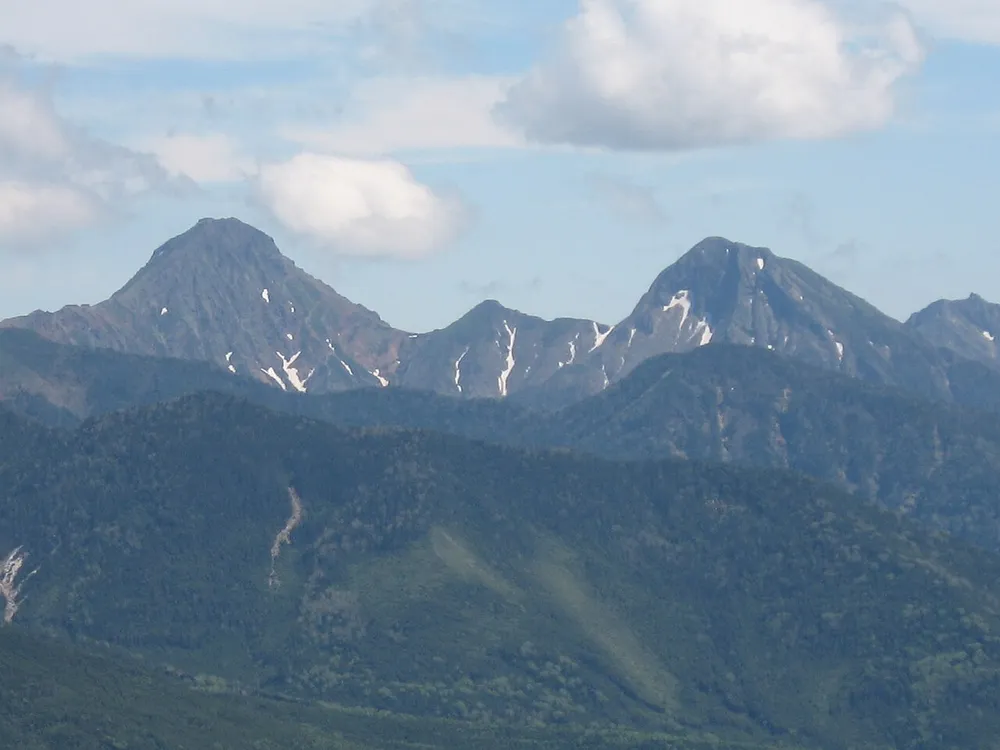 北横岳から見た赤岳と阿弥陀岳。山肌に雪が残り、空には雲がかかっている